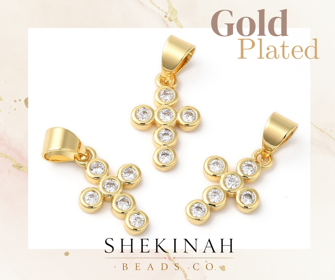 Dije en forma de cruz con acabado dorado y detalles brillantes estilo zirconia.