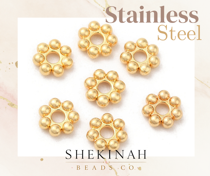 Separadores dorados stainless steel en forma de flor con orificio central para bisutería elegante.